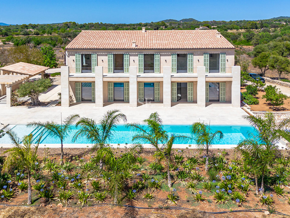 Fachada de villa de lujo con persianas verdes, piscina rectangular y jardín mediterráneo bajo un cielo despejado.
