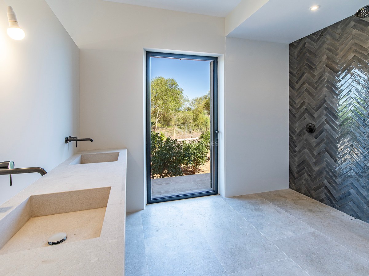 Baño de lujo con lavabo doble de piedra, grifería negra mate y ducha de azulejos en espiga con vistas al jardín.