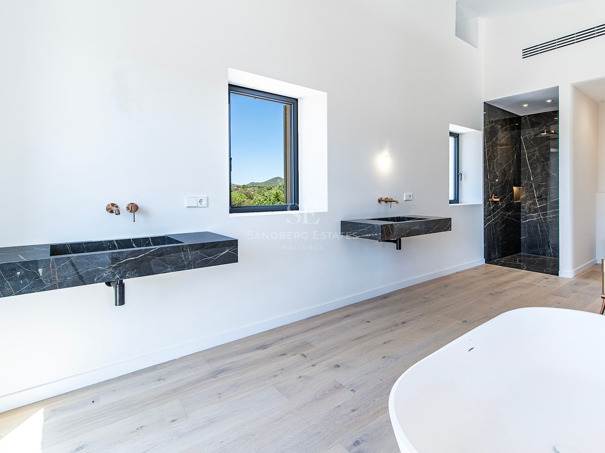Baño principal luminoso con lavabos flotantes de mármol negro, suelos de roble y ducha de mármol.