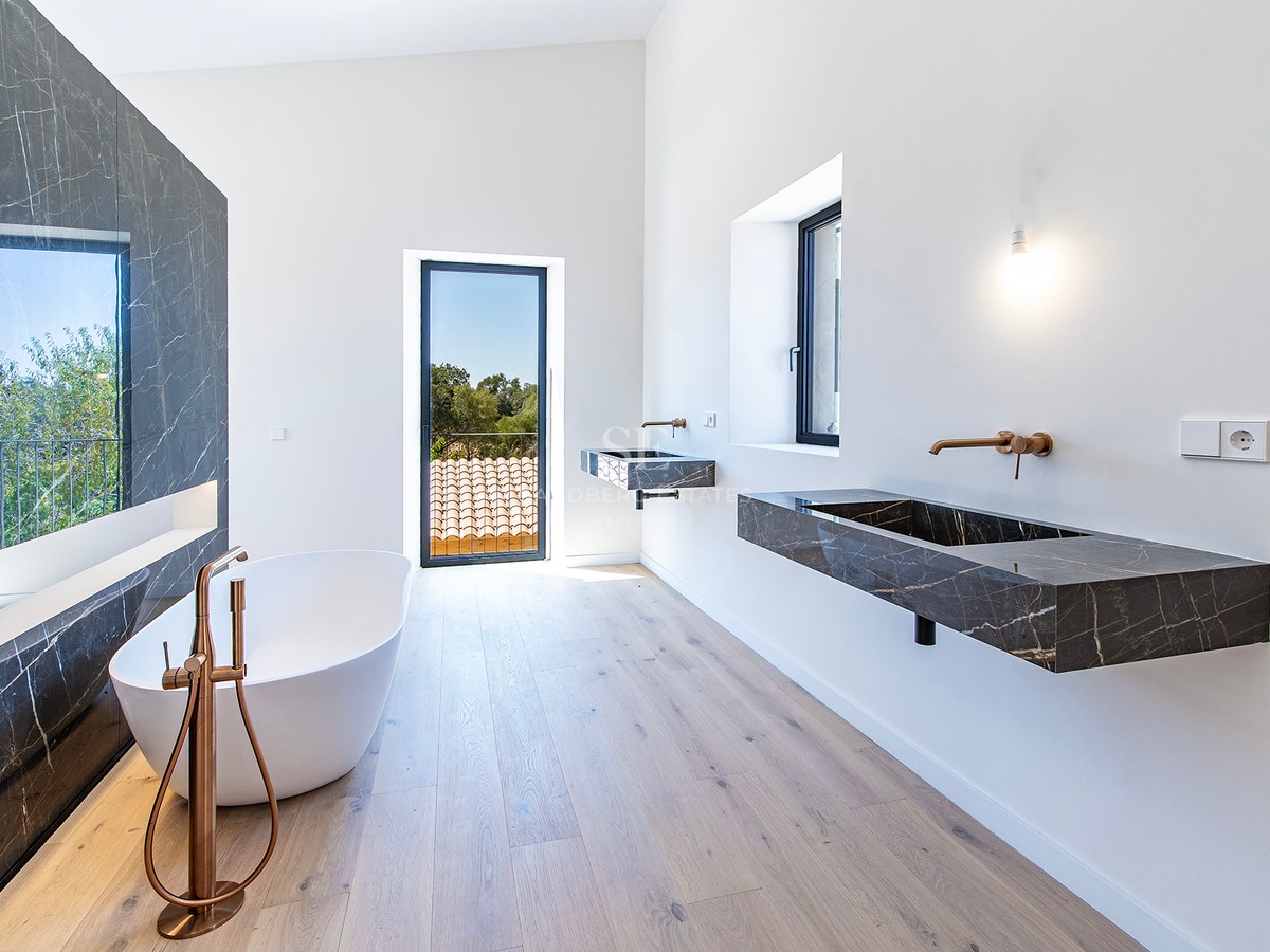 Baño moderno con bañera exenta, pared de mármol oscuro, lavabos suspendidos y grifería de bronce hacia el exterior.