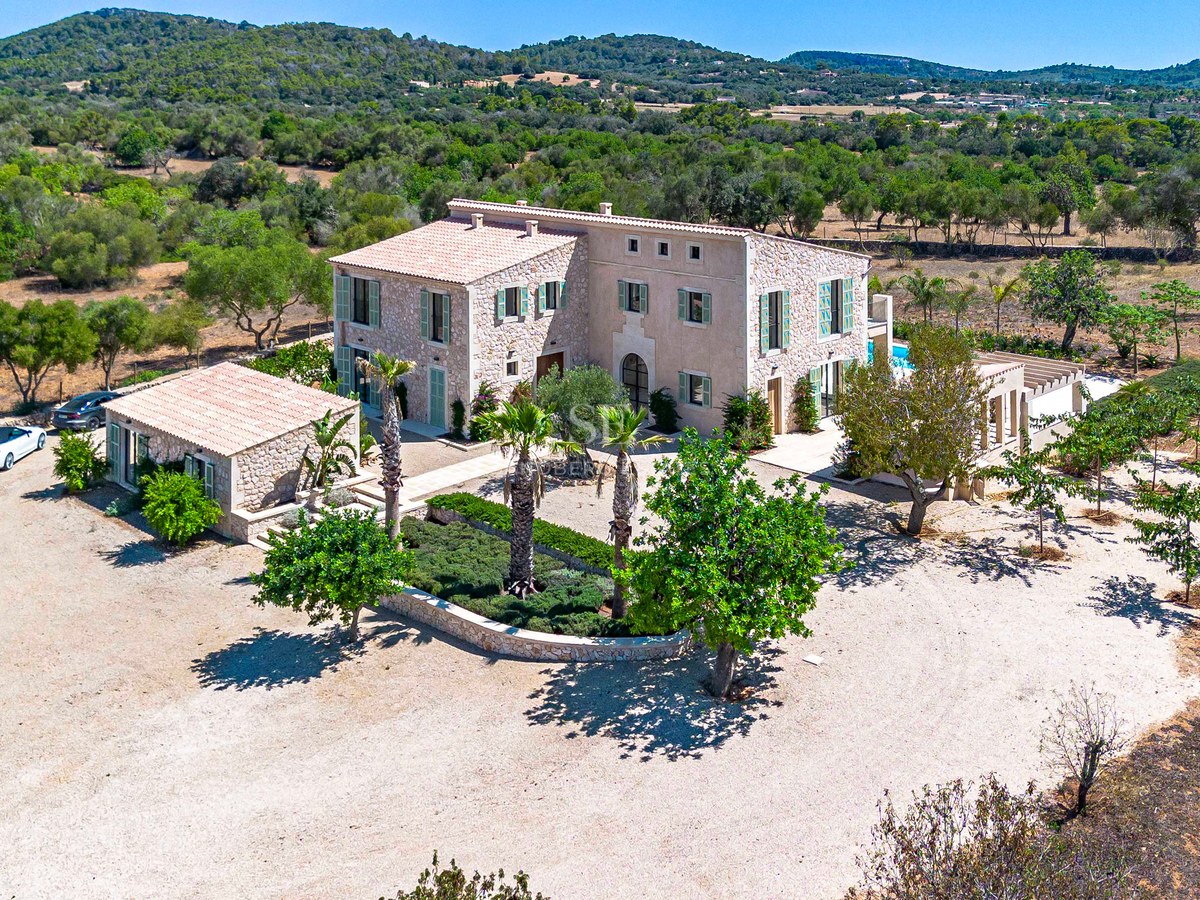 Vista aérea de una gran villa de piedra de dos plantas con casa de invitados, rodeada de paisaje mediterráneo.