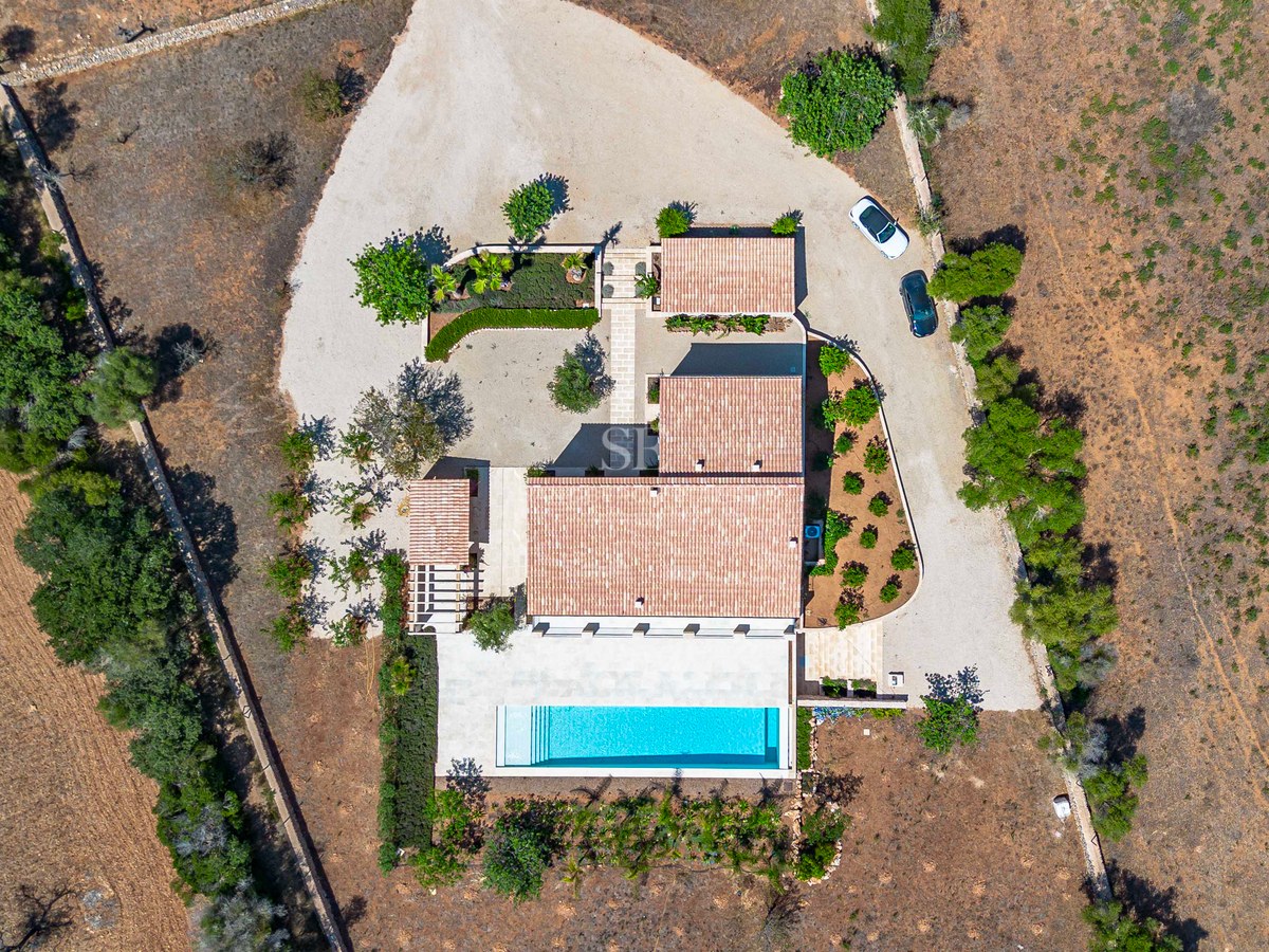 Vista cenital de una villa mediterránea con piscina, tejados de terracota y terrenos privados en el campo.