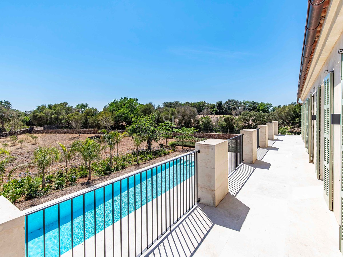 Vista desde terraza de piedra con barandilla negra hacia una piscina alargada y paisaje mediterráneo bajo cielo despejado.