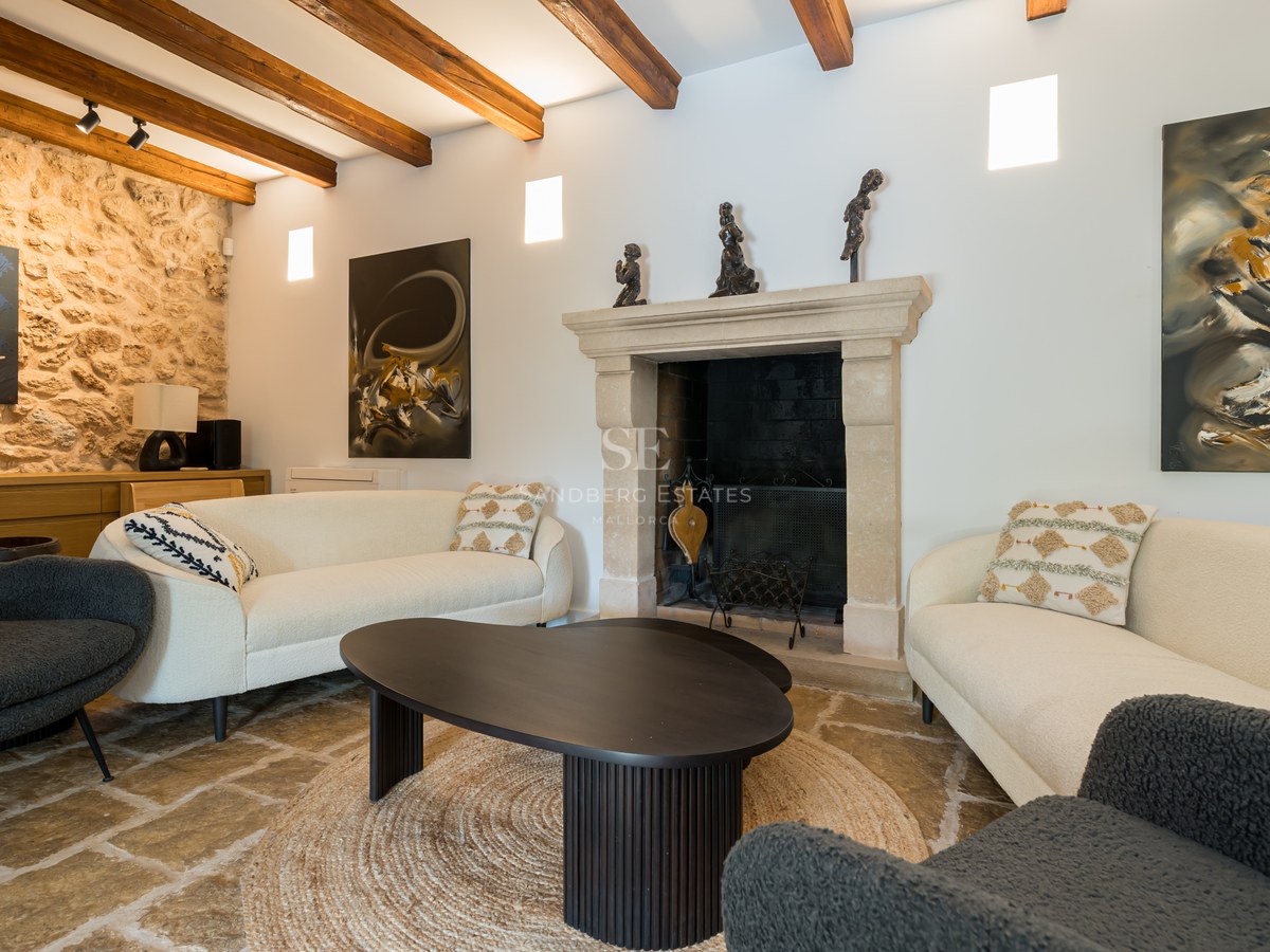 Modern living room with white sofas, stone fireplace, exposed wooden beams, and natural stone flooring.