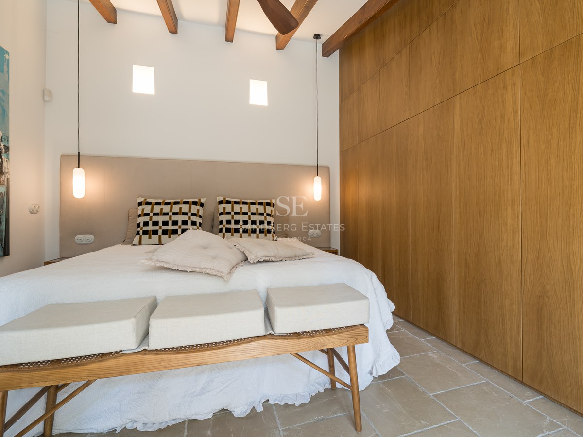 Modern bedroom featuring wood beam ceilings, large oak wardrobes, stone floors, and a blue abstract painting.
