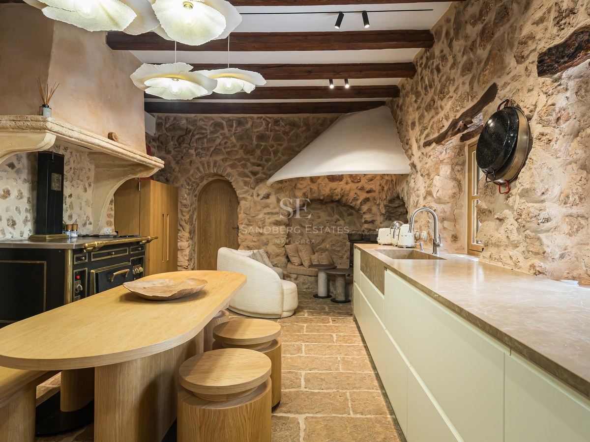 Luxury rustic kitchen with exposed stone walls, wooden beams, a custom oak island, and a vintage-style range cooker.