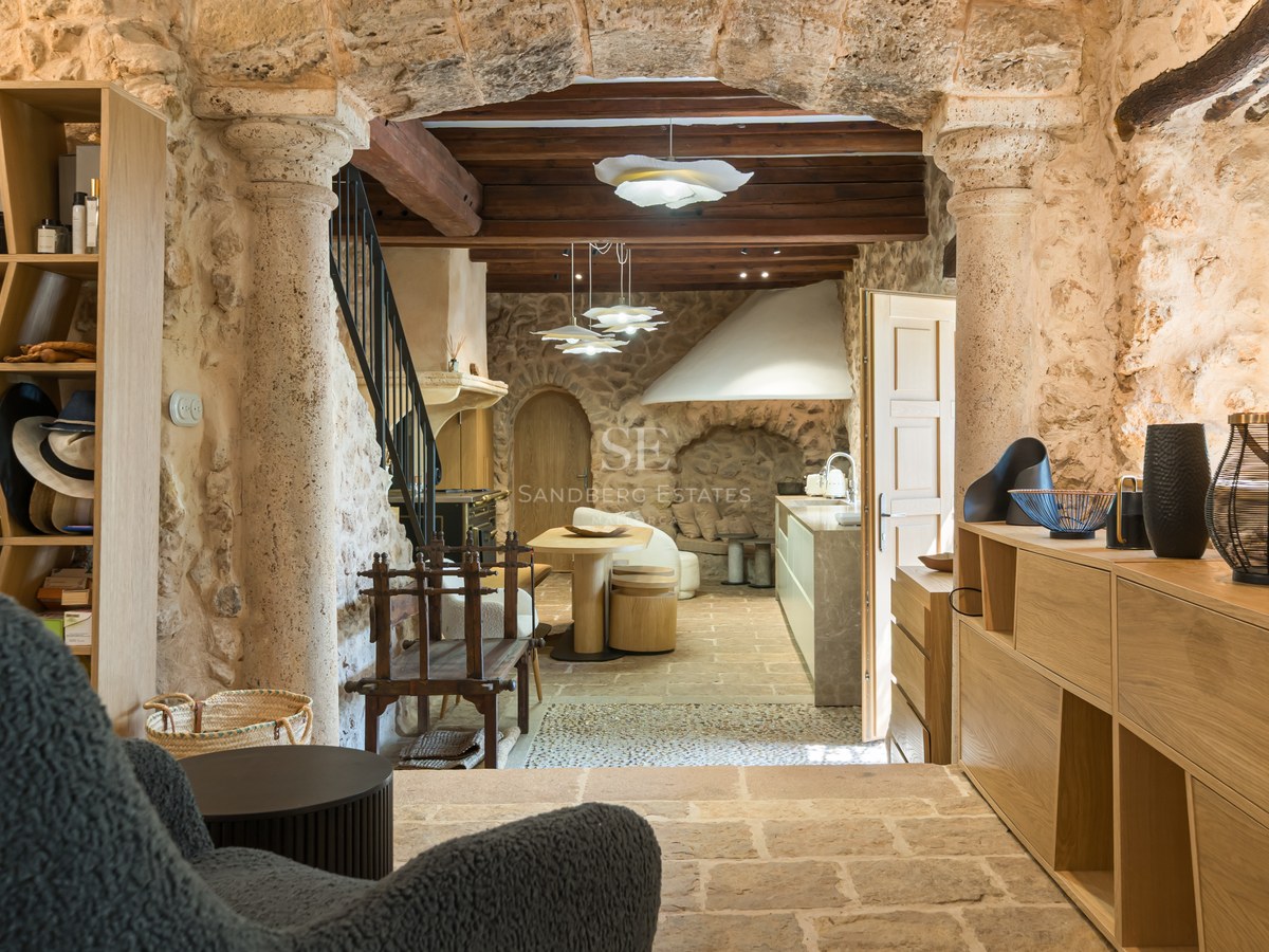 Interior view through a natural stone archway of a rustic kitchen with exposed wood beams and contemporary cabinetry.