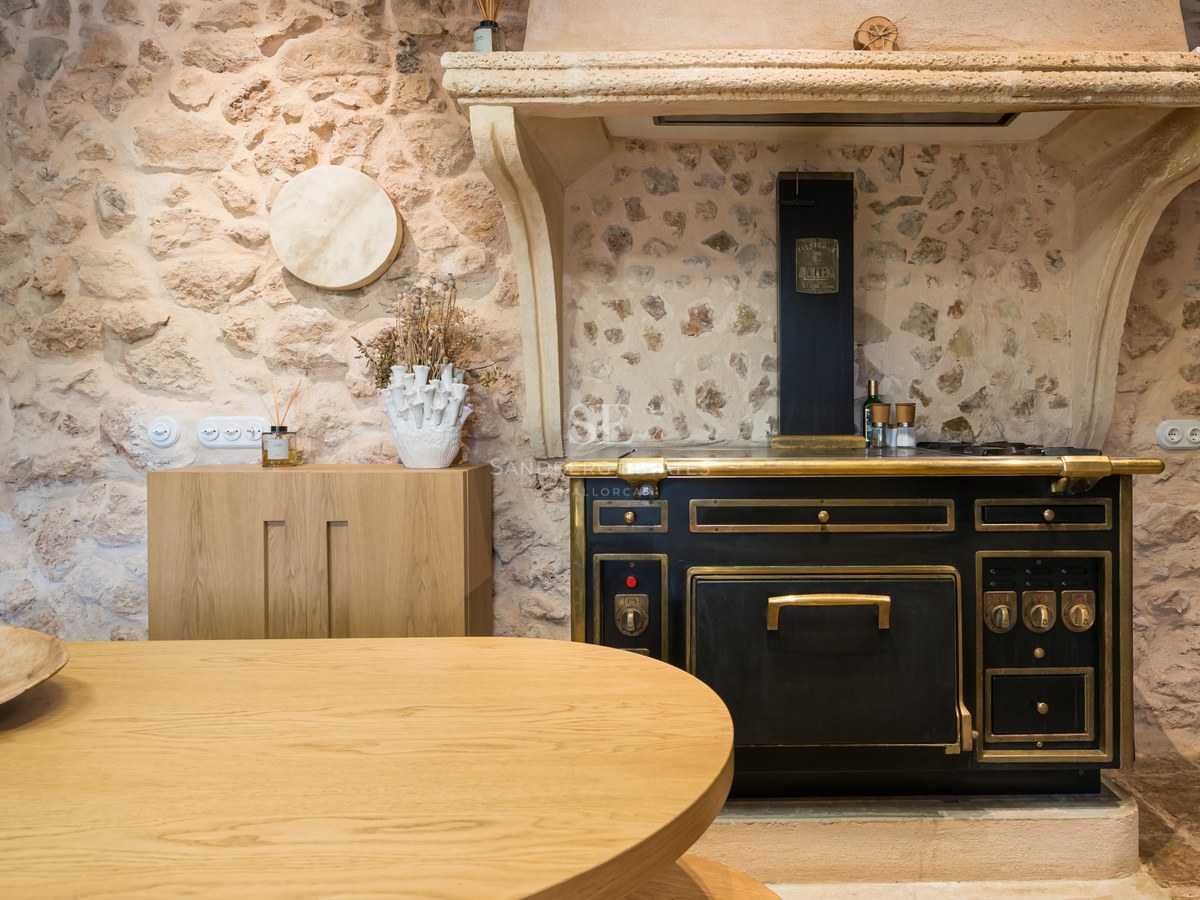 Bespoke black and brass Molteni stove set against a rustic natural stone wall in a luxury Mediterranean kitchen.