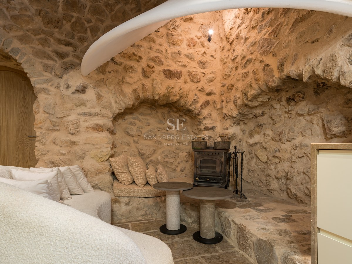 Rustic interior lounge featuring exposed natural stone walls, a stone arch, curved white sofa, and a traditional iron stove.