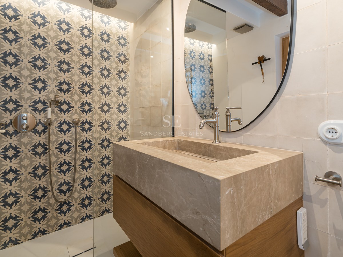 Modern bathroom featuring a large stone vanity, circular mirror, and walk-in shower with blue patterned tiles.