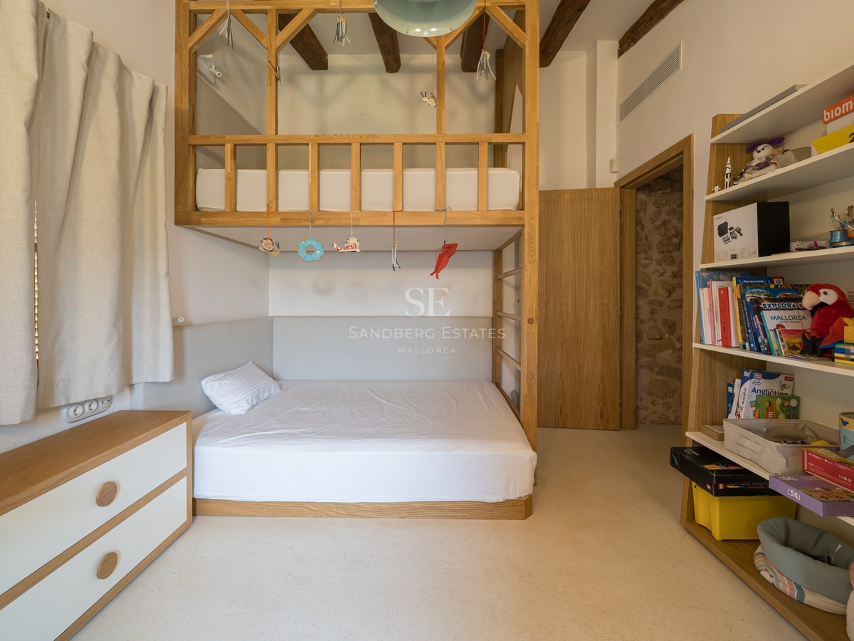 A light-filled children's bedroom featuring custom oak bunk beds, exposed ceiling beams, and integrated shelving.