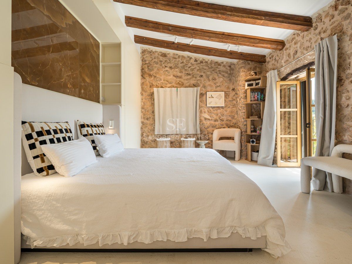 Spacious master bedroom featuring exposed natural stone walls, wooden ceiling beams, and a marble headboard panel.