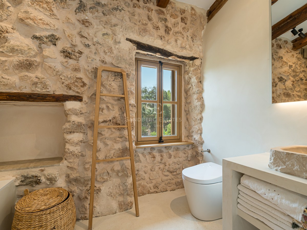 A luxurious bathroom featuring exposed natural stone walls, a hand-carved stone sink, and rustic wooden beams.