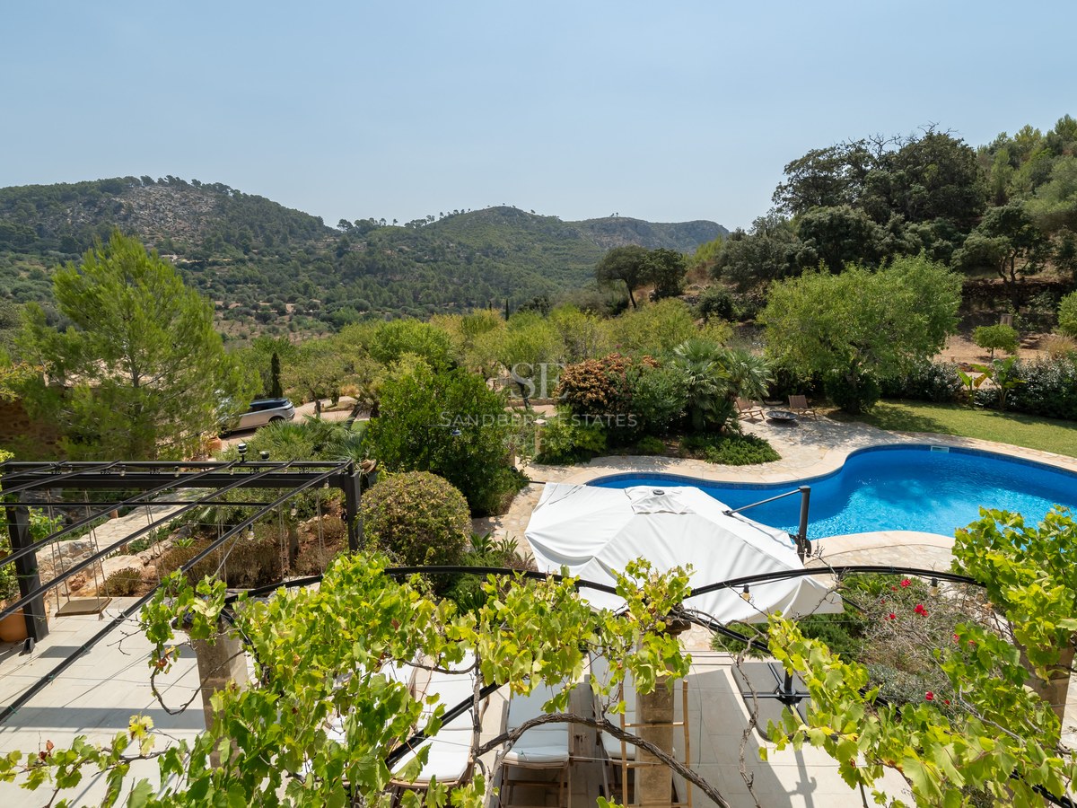 Elevated view of a blue kidney-shaped pool, stone terrace, and lush gardens with green mountains in the distance.