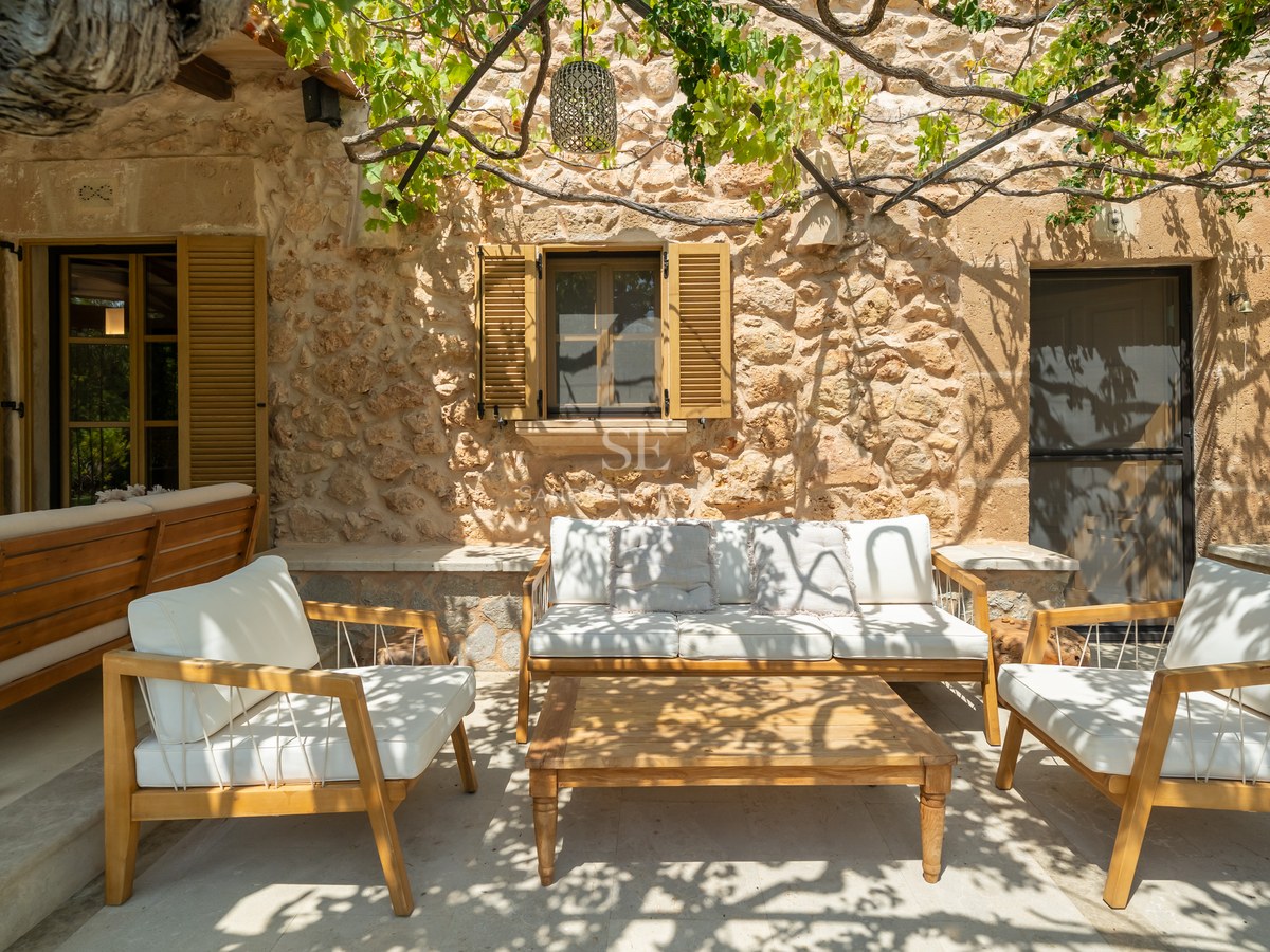 Sun-drenched terrace with wooden lounge furniture, natural stone walls, and a grapevine-covered pergola.