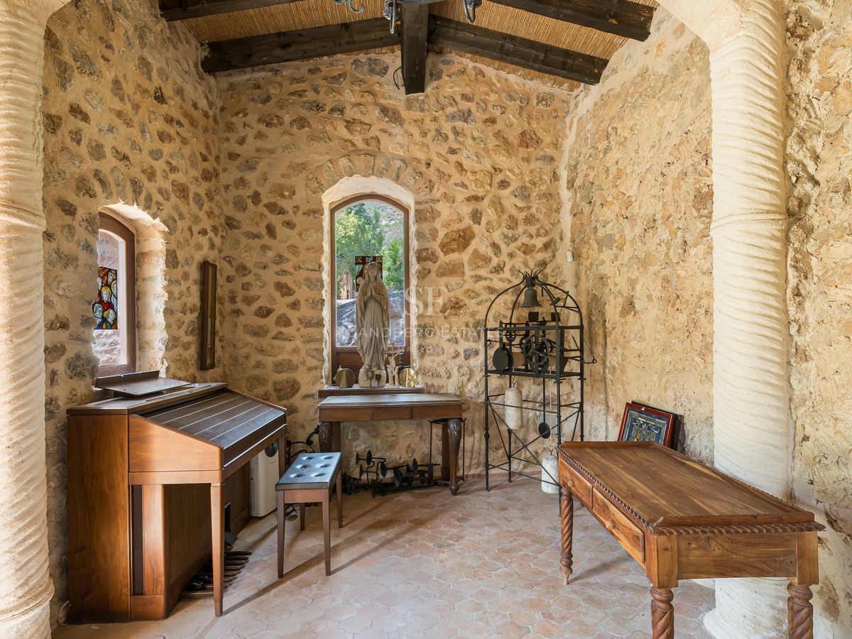 Interior of a traditional stone chapel featuring a wooden organ, religious statue, and vaulted timber ceiling.