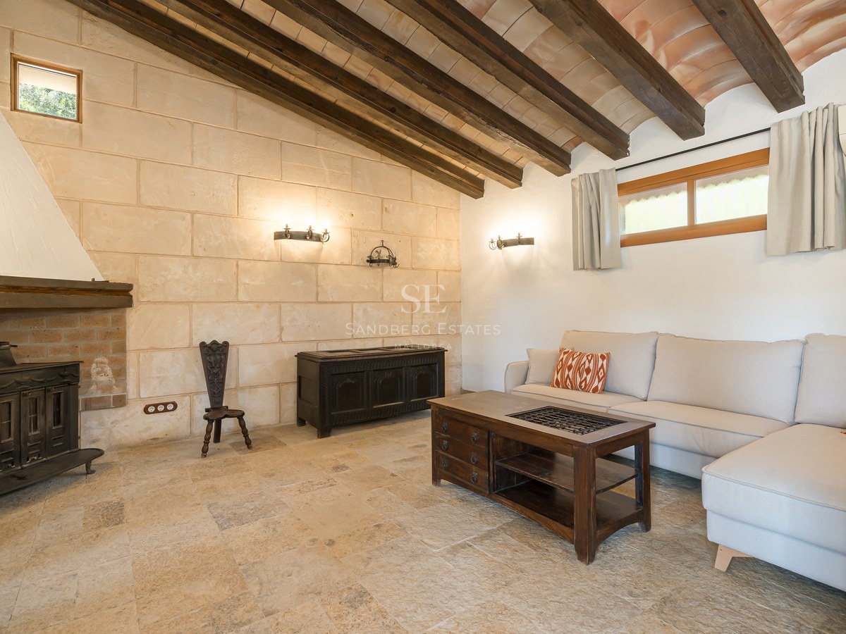 Rustic living room featuring a stone fireplace, exposed wooden ceiling beams, stone floors, and a modern beige sofa.