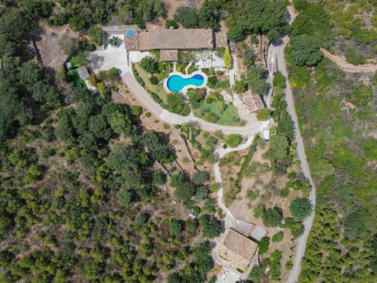 Vista aérea de una villa con tejados de terracota, piscina azul y jardines rodeados de bosque denso.
