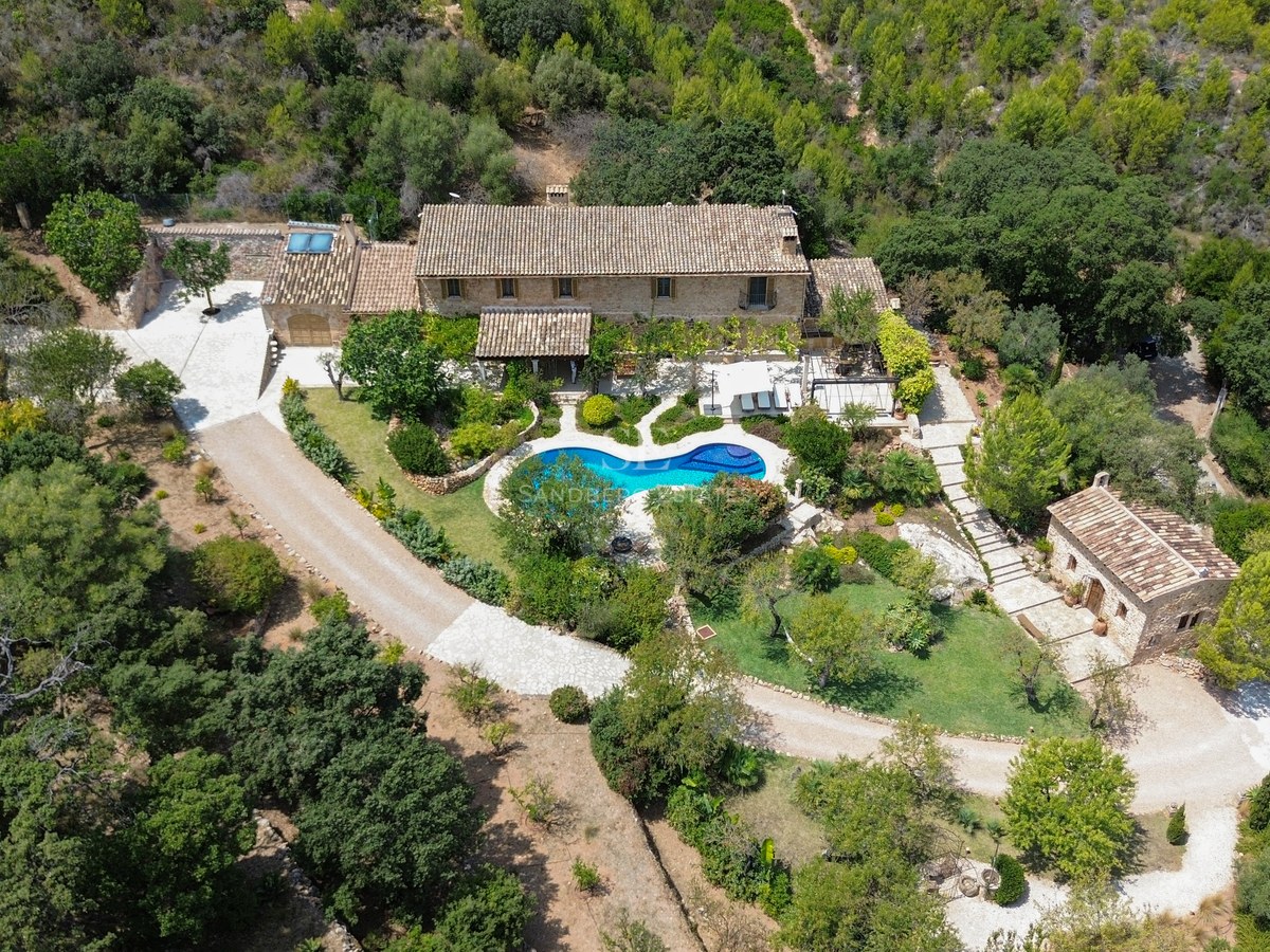 Vista aérea de una villa de piedra con piscina privada rodeada de frondoso bosque mediterráneo.