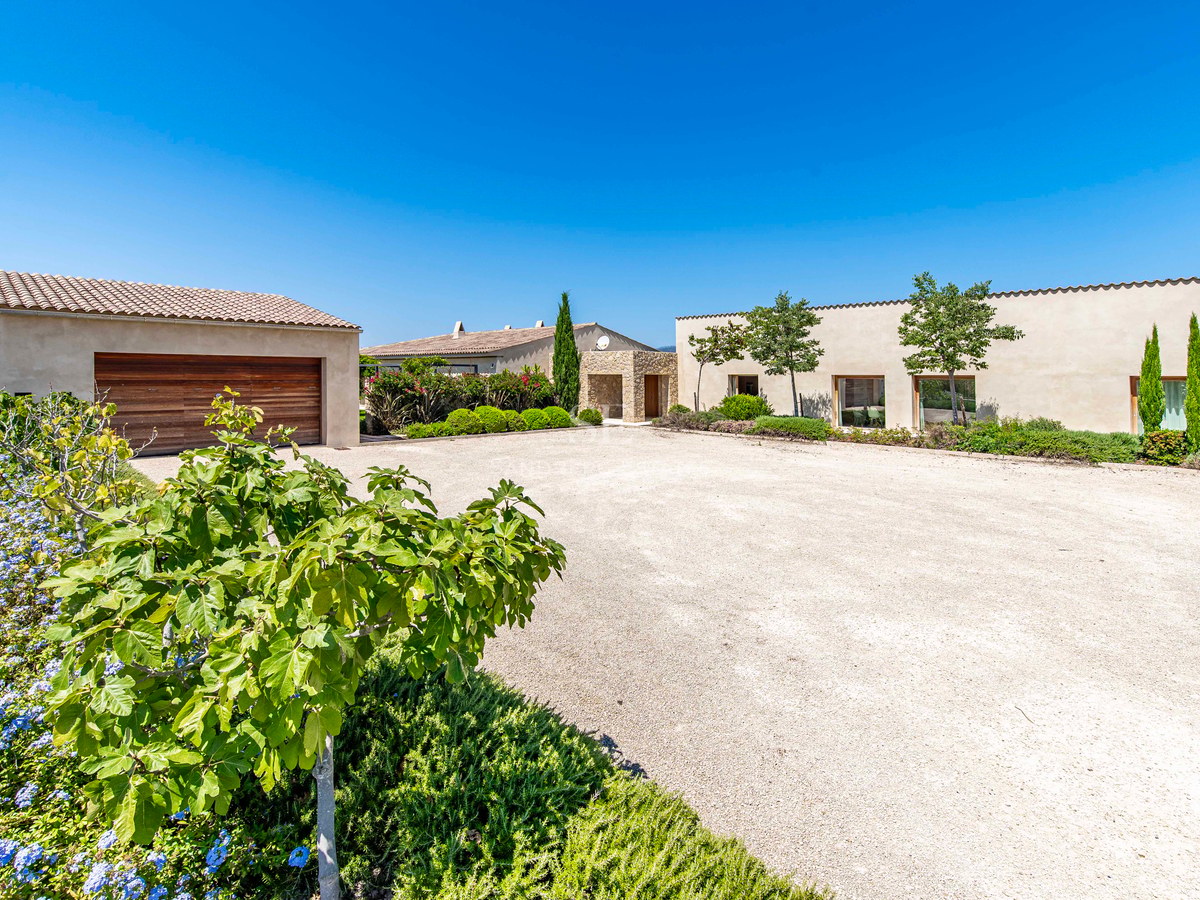 Large allée en gravier menant à une villa méditerranéenne moderne avec garage en bois et jardins paysagers.