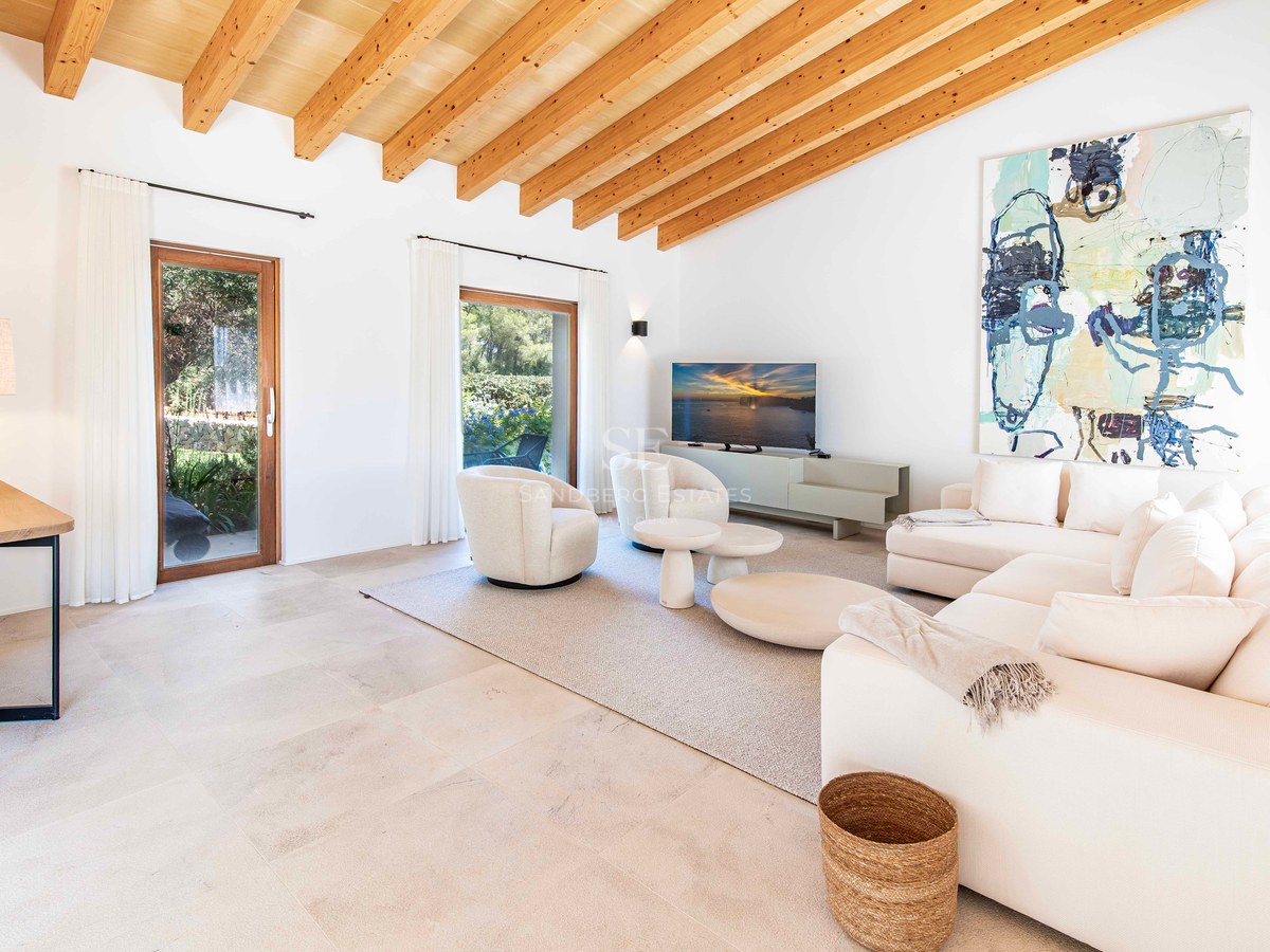 Salon moderne avec haut plafond à poutres, canapés blancs, sol en pierre naturelle et accès au jardin.