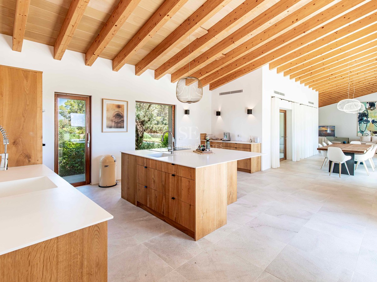 Cuisine spacieuse avec îlot en chêne, plans de travail blancs, poutres apparentes au plafond et sol en pierre.