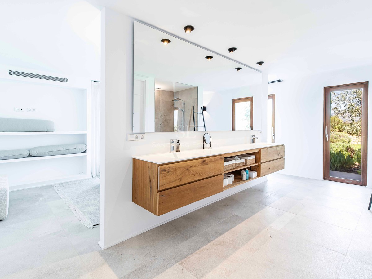 Salle de bains moderne avec double vasque suspendue en chêne, grand miroir et porte vitrée sur jardin.