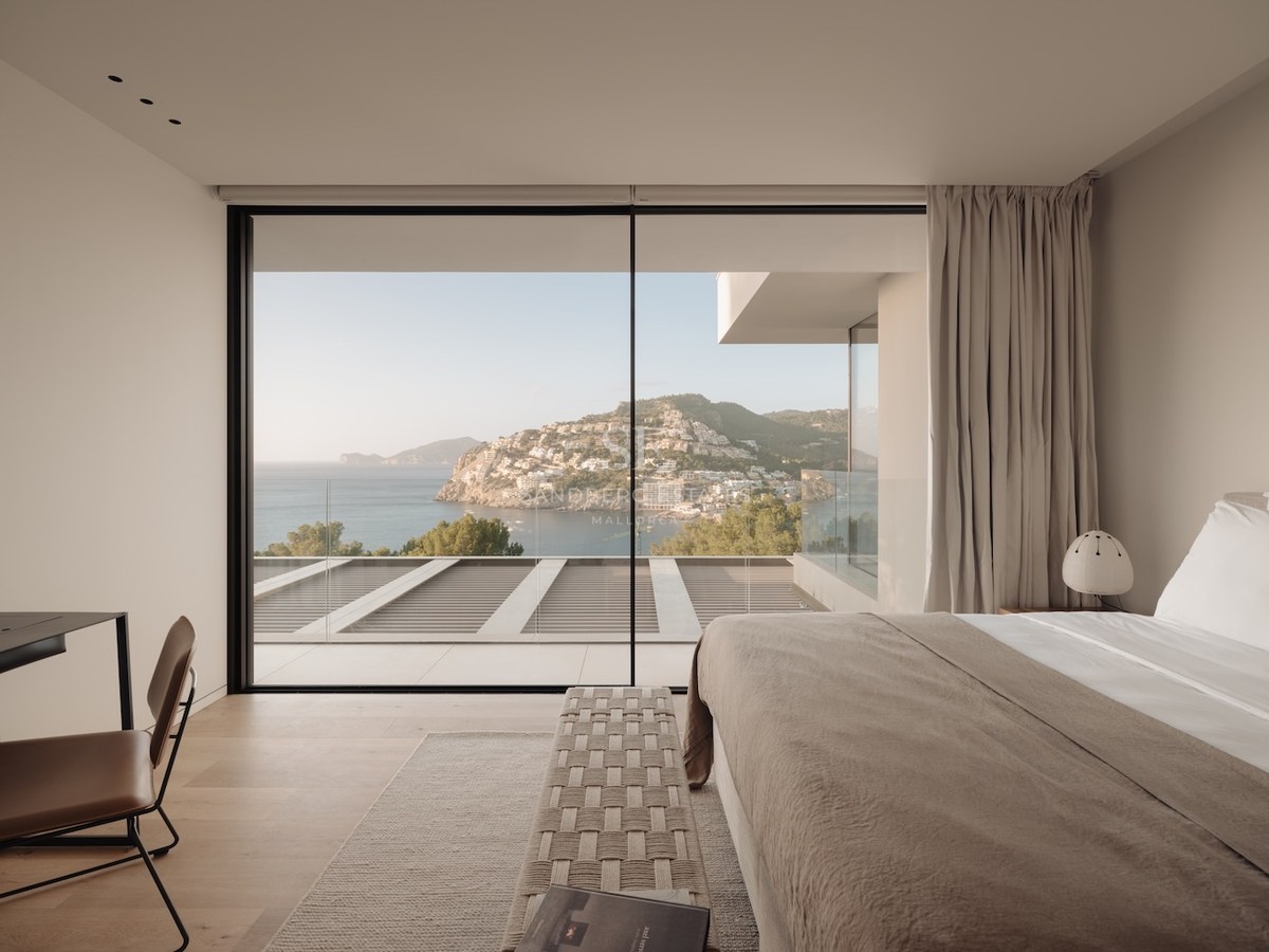 Dormitorio de lujo con ventanales de suelo a techo y vistas panorámicas a una bahía mediterránea.