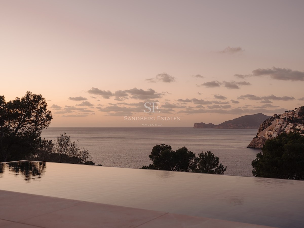 Piscina infinita reflejando un cielo rosado al atardecer con vistas a la costa y el mar Mediterráneo.