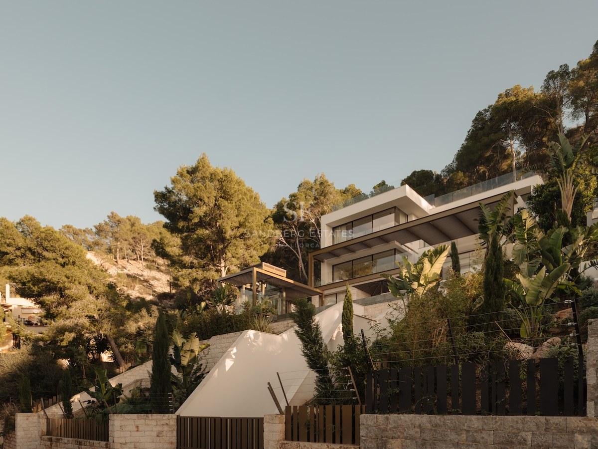 Villa moderna de varios niveles en color blanco integrada en una colina con grandes ventanales y vegetación mediterránea.