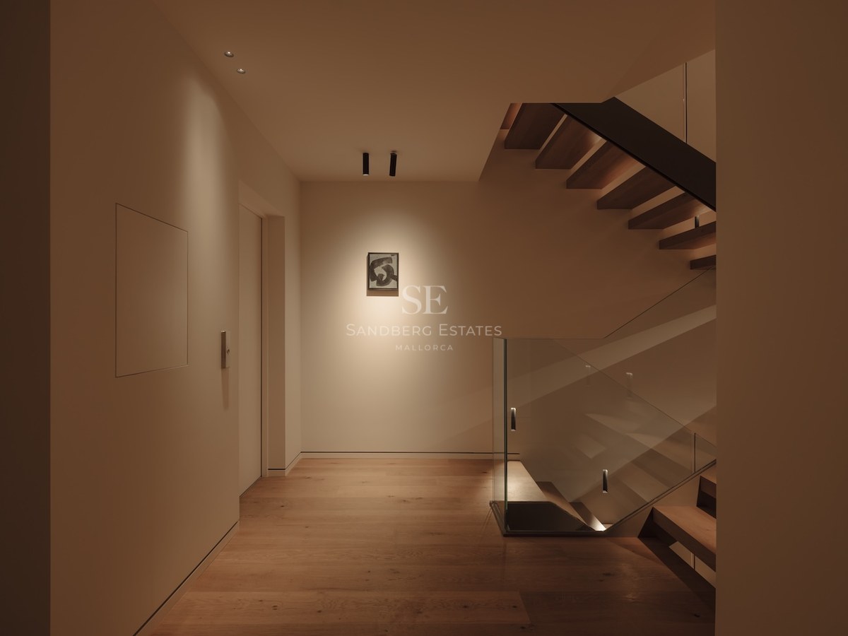 Escalera moderna de madera con barandillas de cristal e iluminación cálida empotrada en un pasillo minimalista.