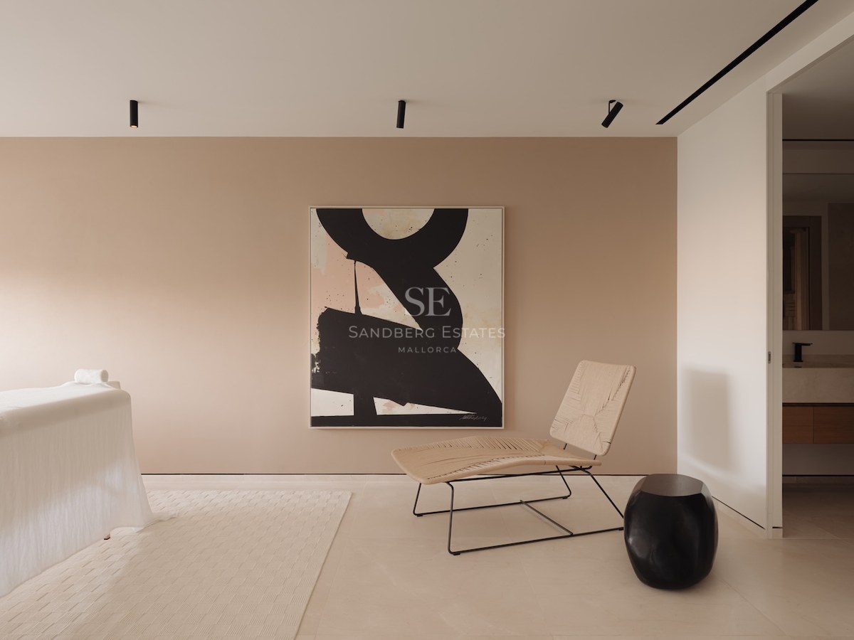 Sala de spa minimalista con mesa de masaje, silla de diseño tejida, arte abstracto y paredes en tonos arena.