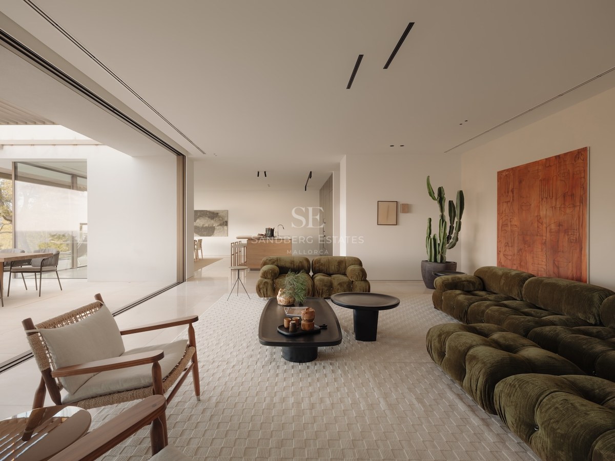 Salón moderno con sofás de terciopelo verde oliva y grandes ventanales que dan a una terraza luminosa.