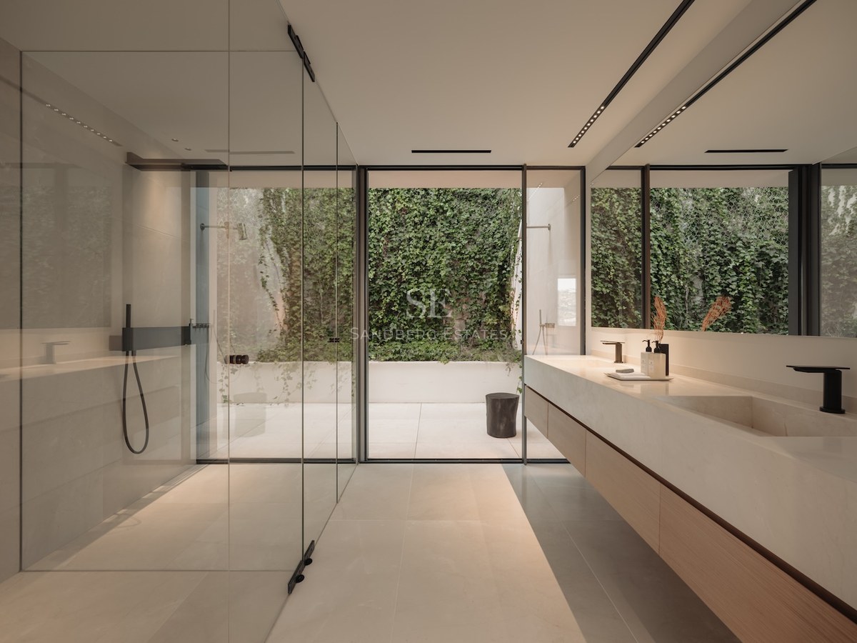 Baño moderno con amplia ducha de cristal, lavabo de piedra y vistas a un patio privado con muro verde.