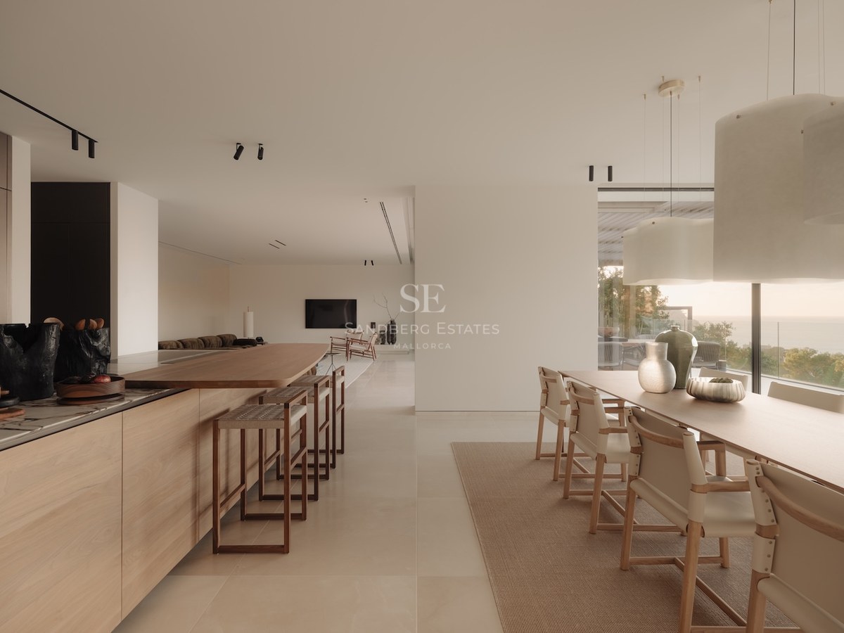 Cocina moderna de concepto abierto con muebles de roble, isla de mármol y grandes ventanales con vistas al mar.