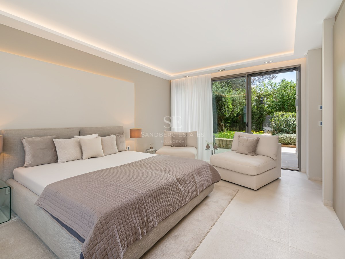 Contemporary bedroom with neutral tones, large bed, glass bedside table, and sliding doors opening to a lush garden.