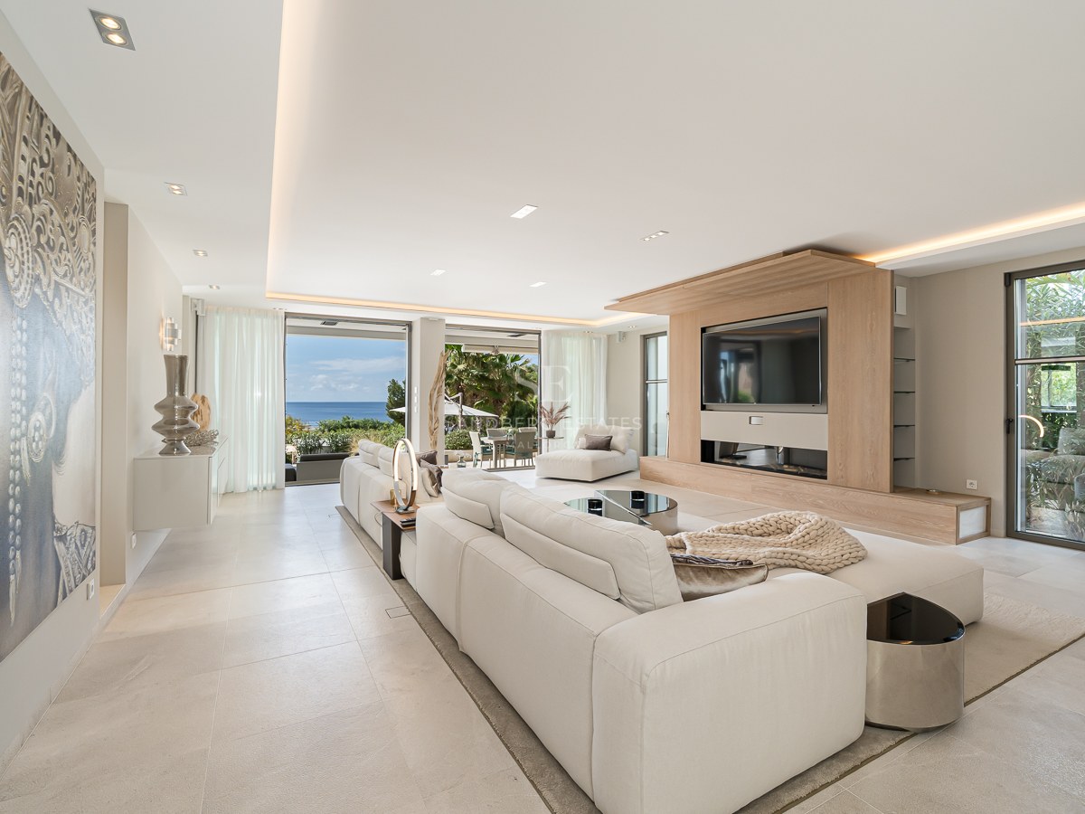 Modern living room with white sectional sofa, large wall mural, and glass doors opening to a sea-view terrace.