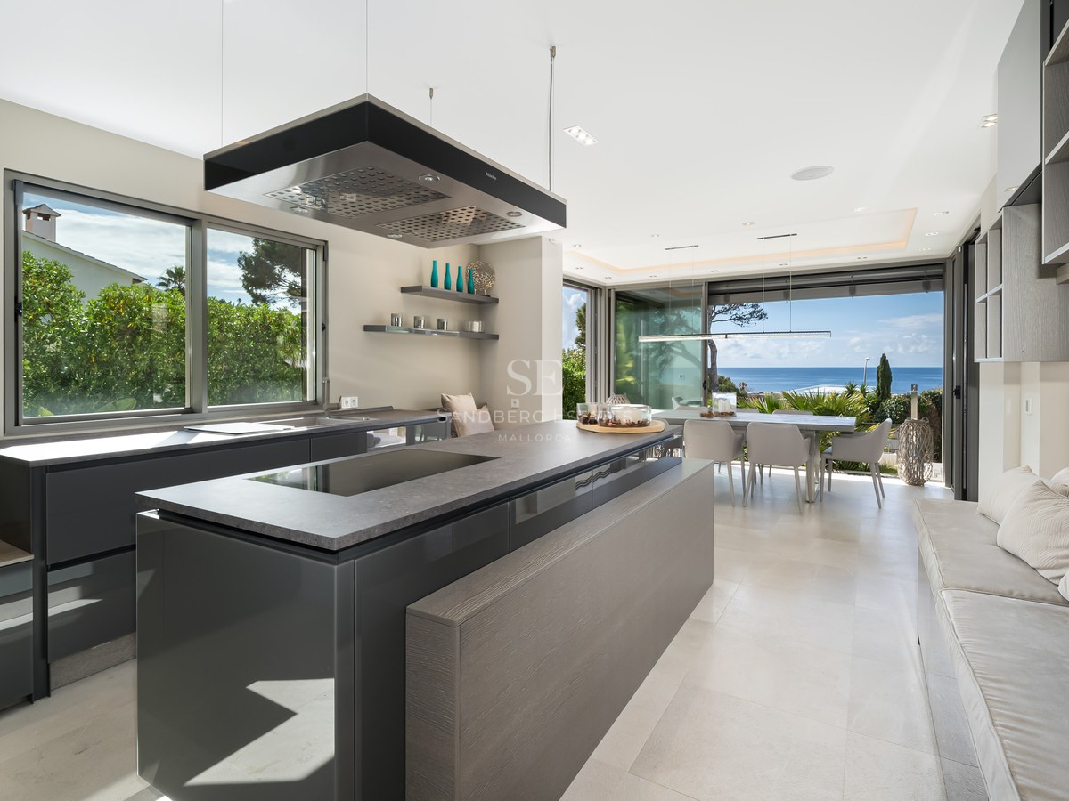 Modern kitchen featuring a charcoal grey island, designer extractor, and floor-to-ceiling windows with Mediterranean views.