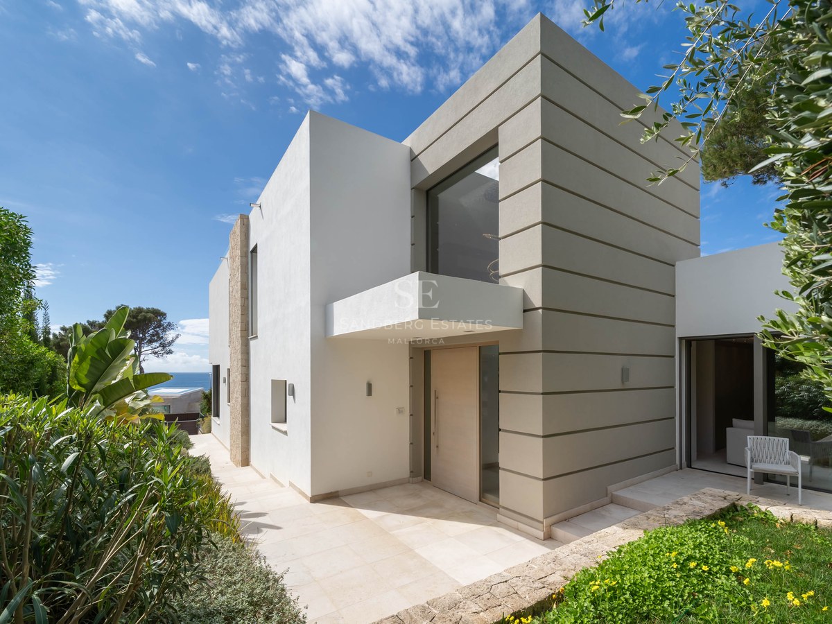 Modern two-story villa facade with white and beige geometric walls, a glass entrance, and Mediterranean landscaping.