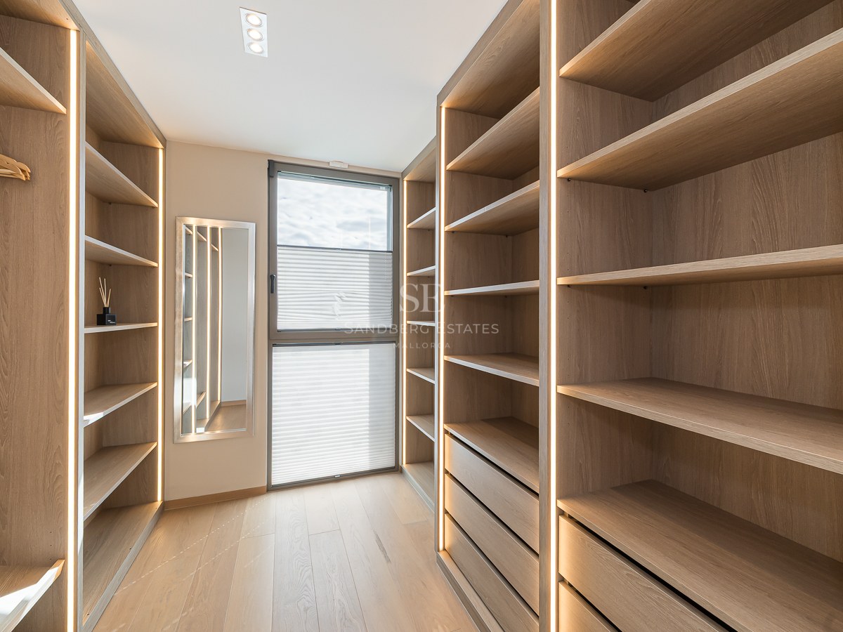 Custom oak-finished walk-in closet with integrated vertical LED lighting and a full-length mirror.