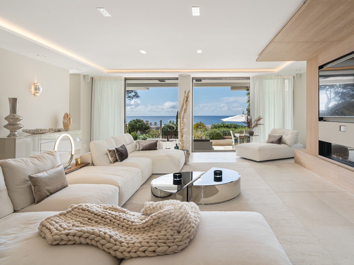 Modern living room with white sofas, oak wood accents, and large glass doors overlooking the Mediterranean Sea.