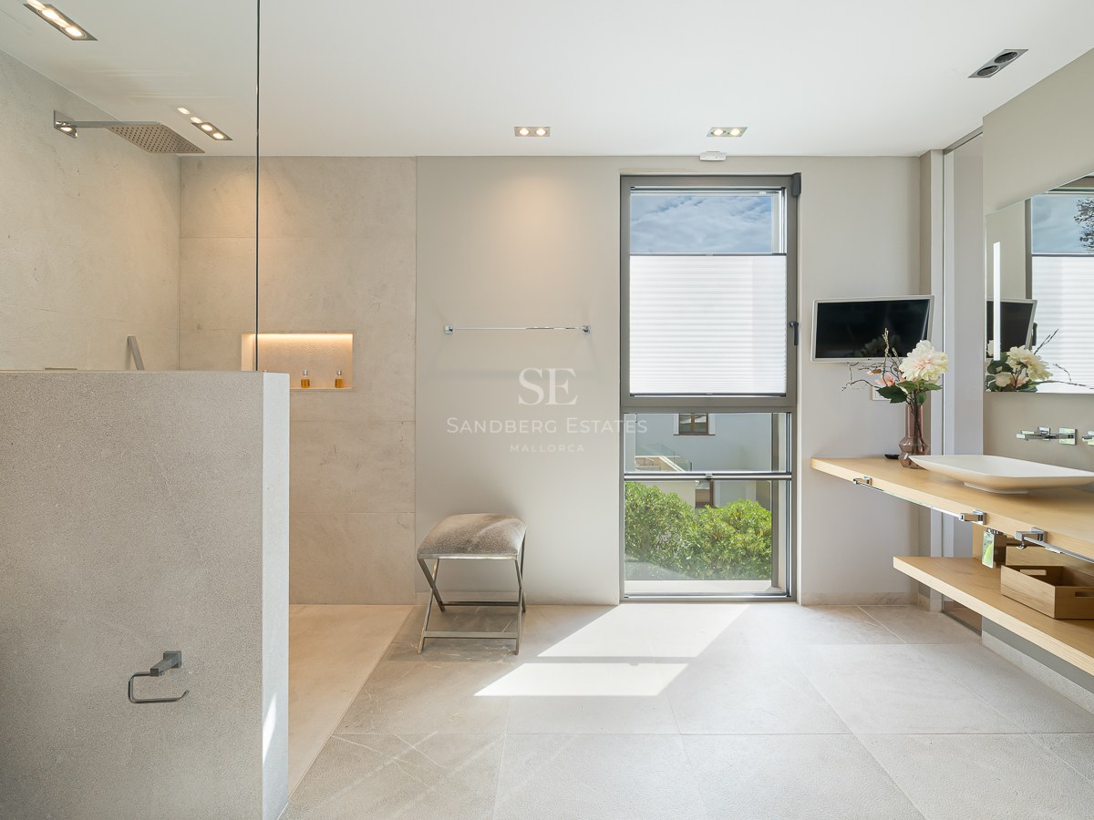 Contemporary bathroom featuring double wooden vanity, beige stone tiling, and glass-enclosed rain shower.
