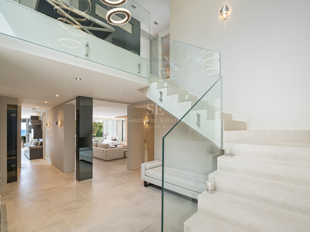 A wide-angle shot of a modern villa entrance featuring a stone staircase with glass balustrades and high ceilings.