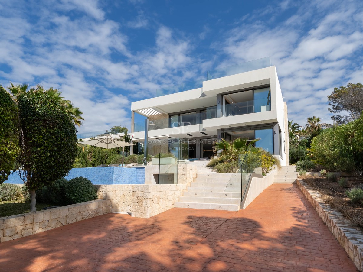 Three-story modern white villa with glass balconies, blue swimming pool, and stone stairs under a bright blue sky.