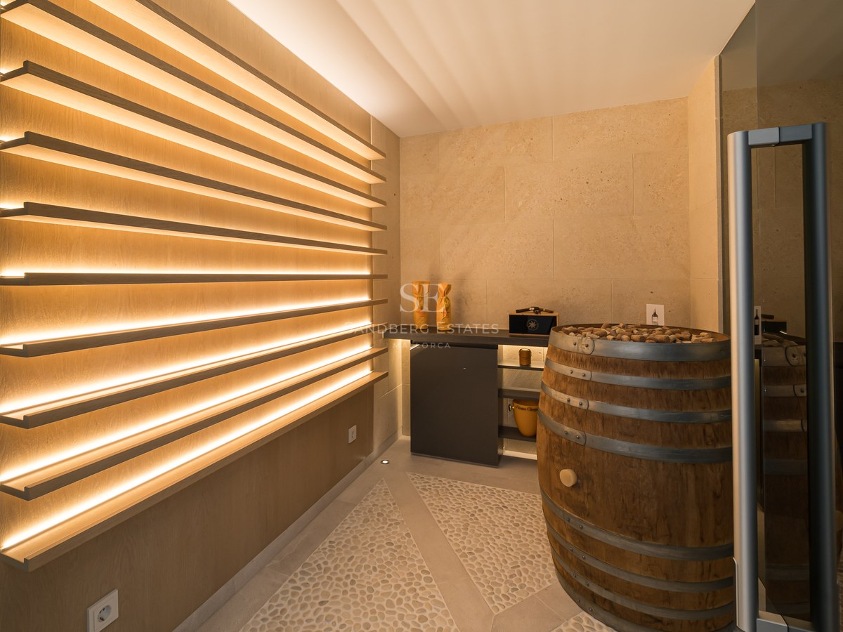 Modern wine cellar featuring backlit oak shelving, limestone walls, and a decorative wine barrel.