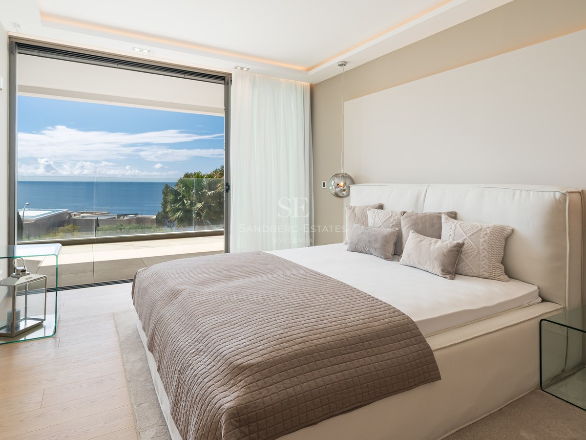 Modern master bedroom featuring white bedding and glass doors opening to a private terrace with Mediterranean Sea views.