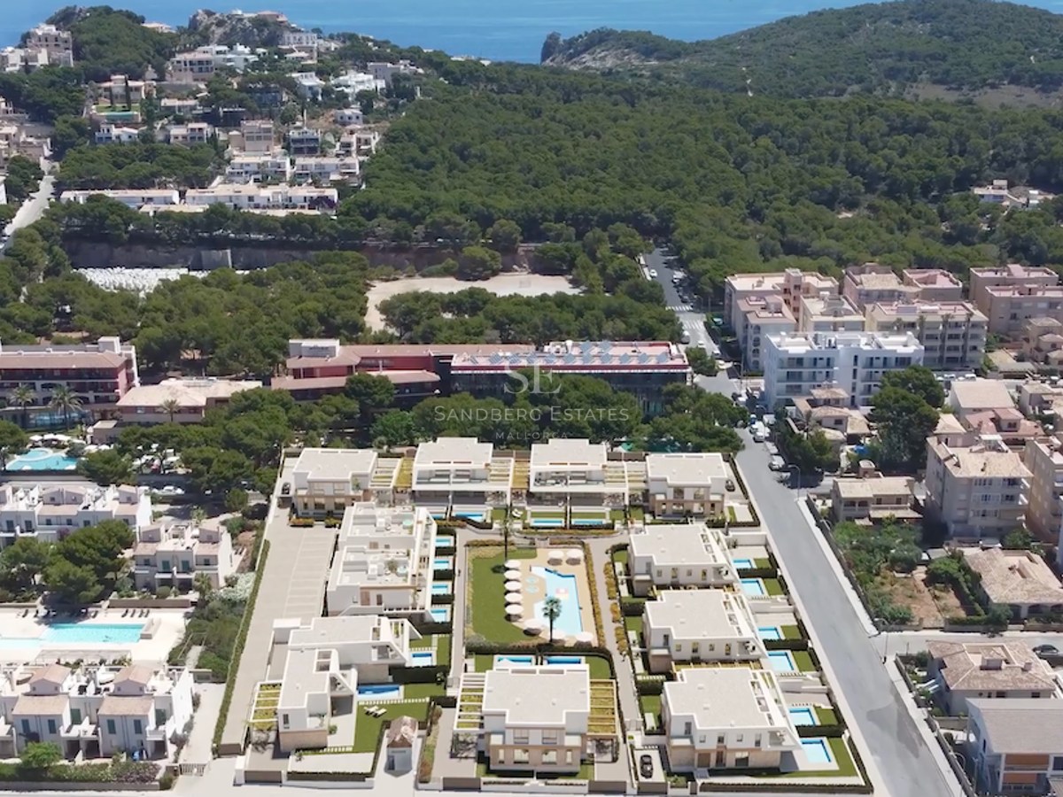 Drohnenaufnahme einer modernen Wohnanlage mit weißen Gebäuden, privaten Pools und üppiger mediterraner Vegetation.
