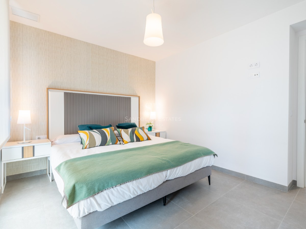 Modernes Schlafzimmer mit großem Bett, grüner Decke, strukturierter Akzentwand und zwei Nachttischlampen.