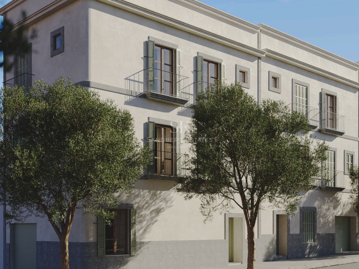 Façade de bâtiment couleur crème avec volets verts, balcons en fer forgé et oliviers sous une lumière naturelle.