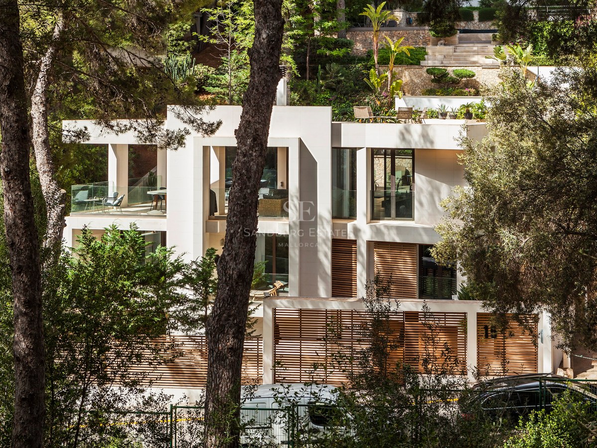 Villa contemporaine à plusieurs niveaux avec façade en pierre, lattes de bois et terrasses en verre entourée de pins.